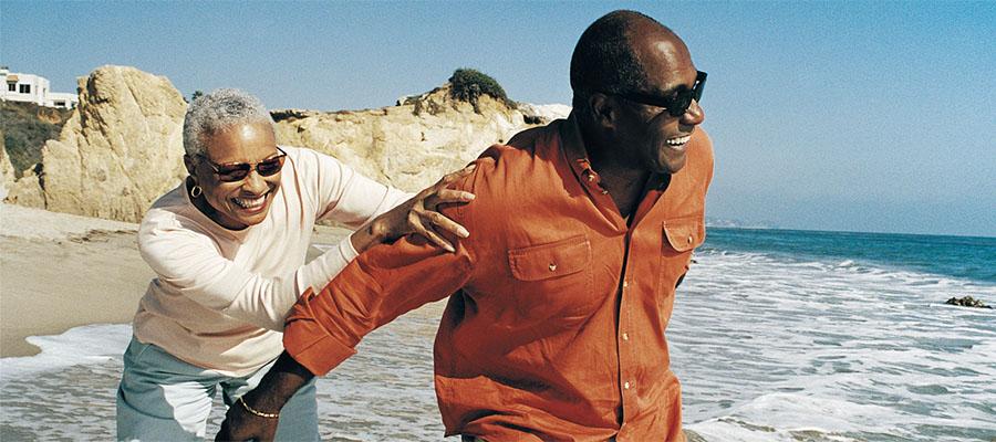 Husband and wife running in the ocean at the beach and laughing