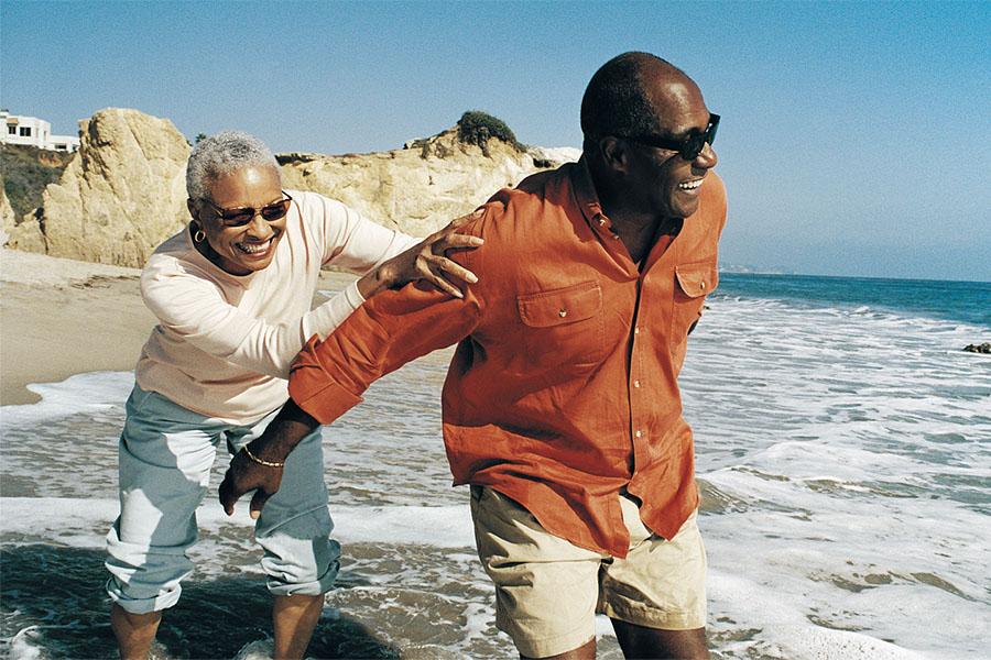 Husband and wife running in the ocean at the beach and laughing