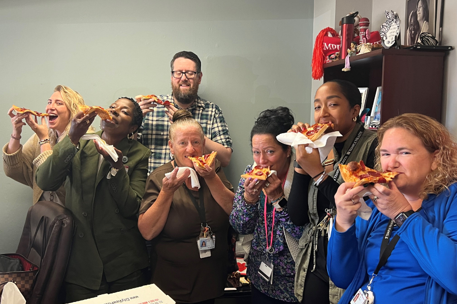Release the Hounds (with Maag, far left, Stinson, second from right, and Hummel, far right) eating pizza in Chaudron Carter-Short (second from left)'s office.
